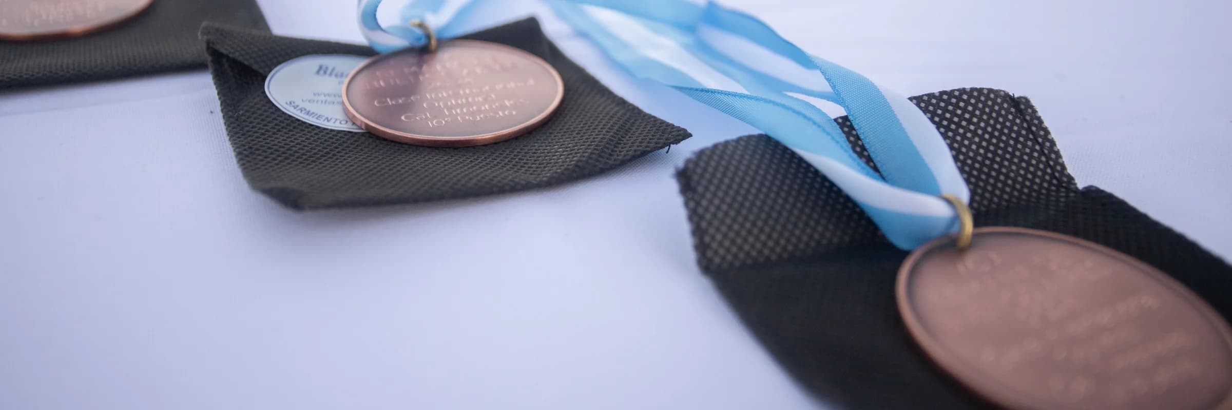 Bronze competition medals on blue and white ribbons laid out on a white table